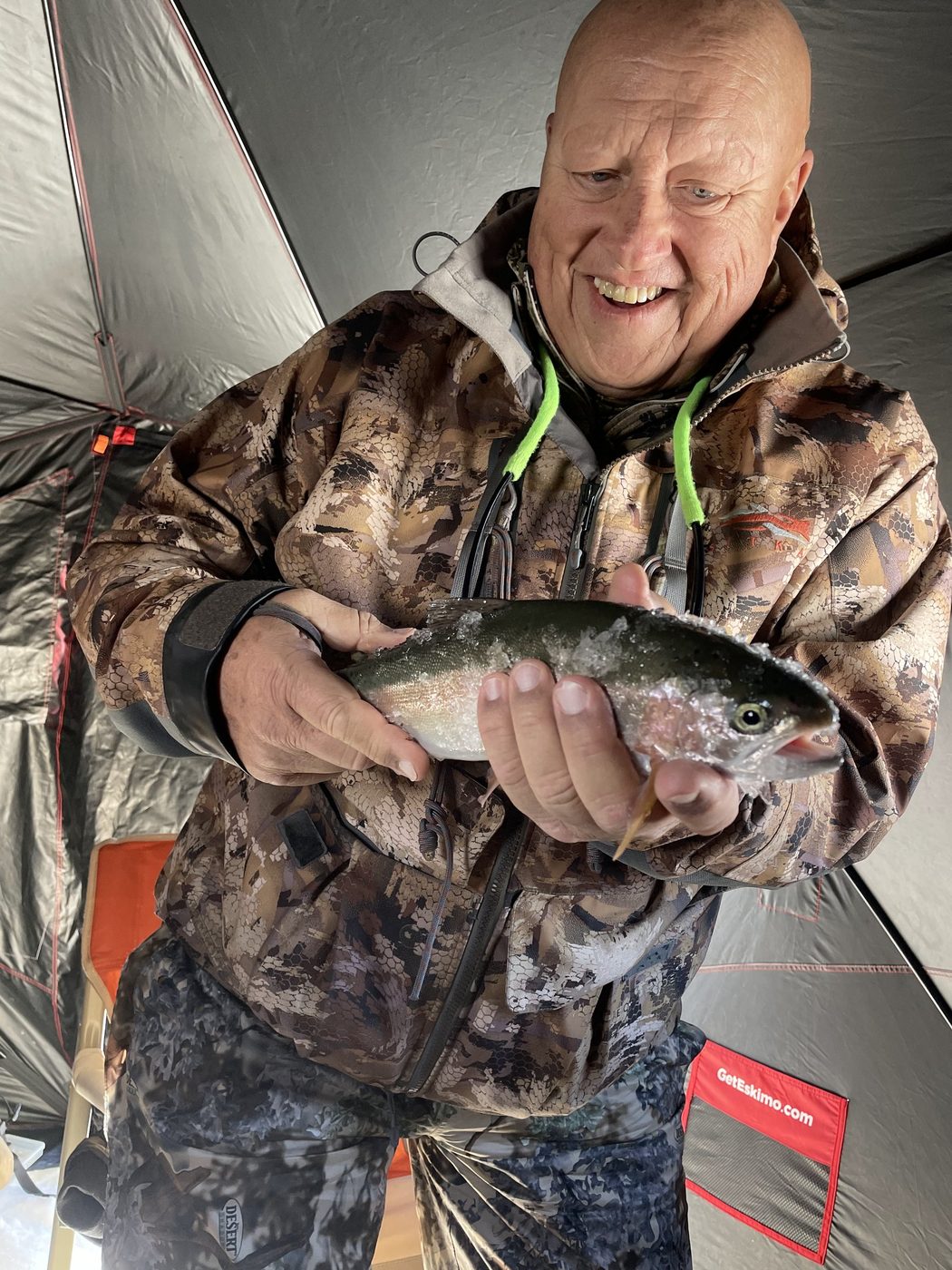 Smiling angler in a camouflage jacket holding a trout