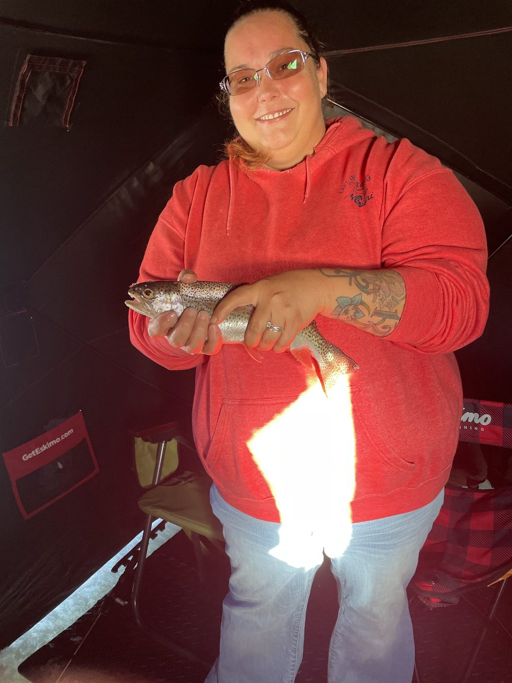 Angler in a red hoodie holding a trout inside an ice shelter