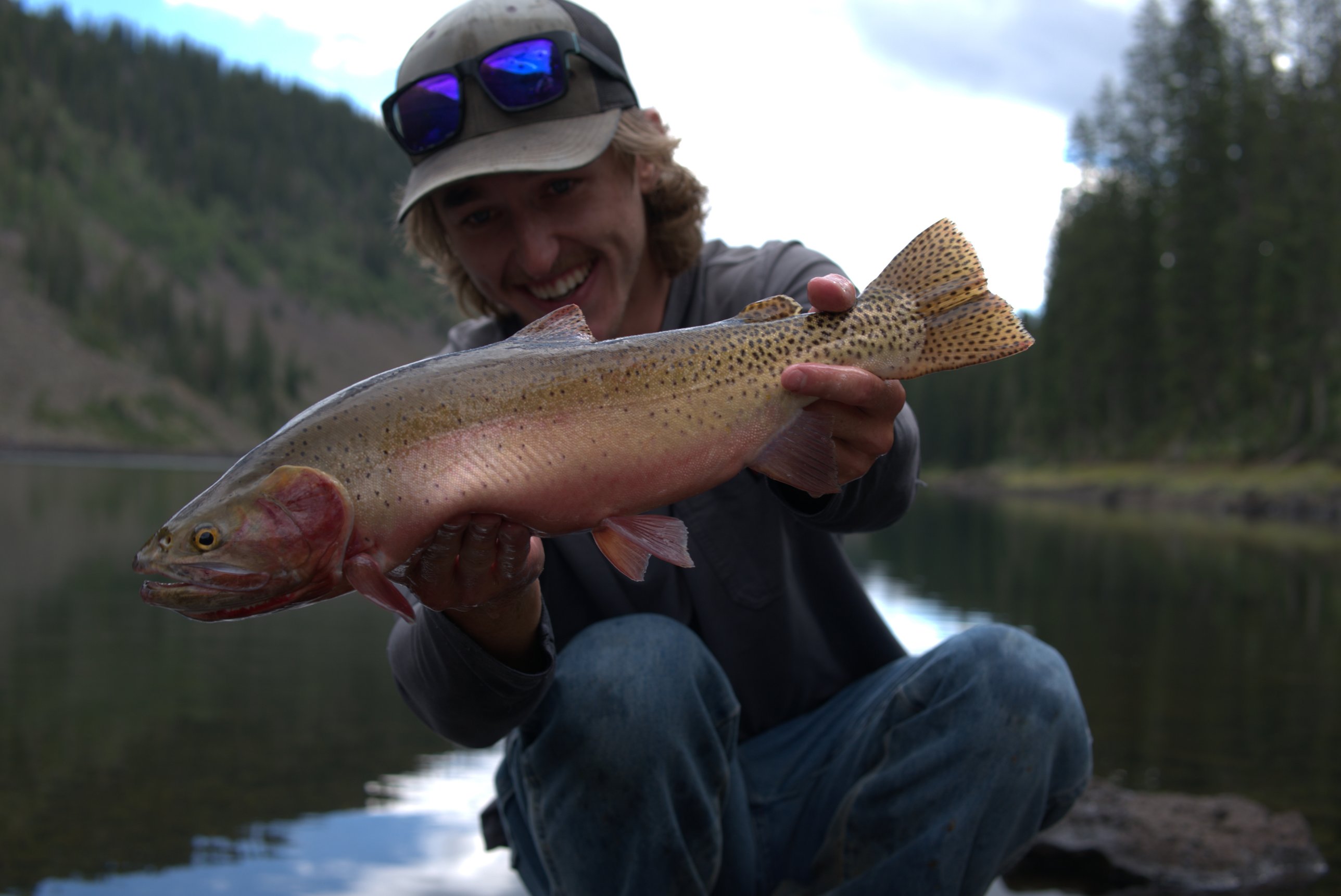 Phoenix Harris smiling while holding a large cutthroat trout beside a mountain lake
